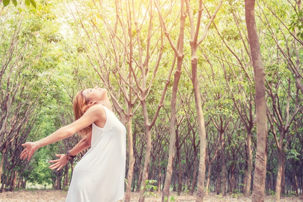 Una ragazza con un vestito bianco si gode la foresta tra gli alberi.
