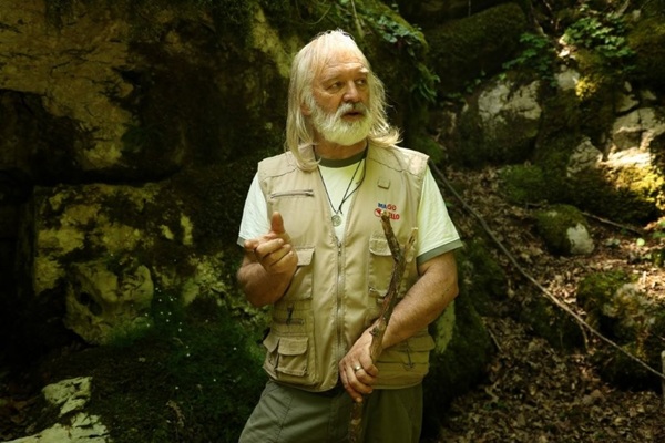 Un uomo anziano, circondato dal verde del bosco e dalle roccie.